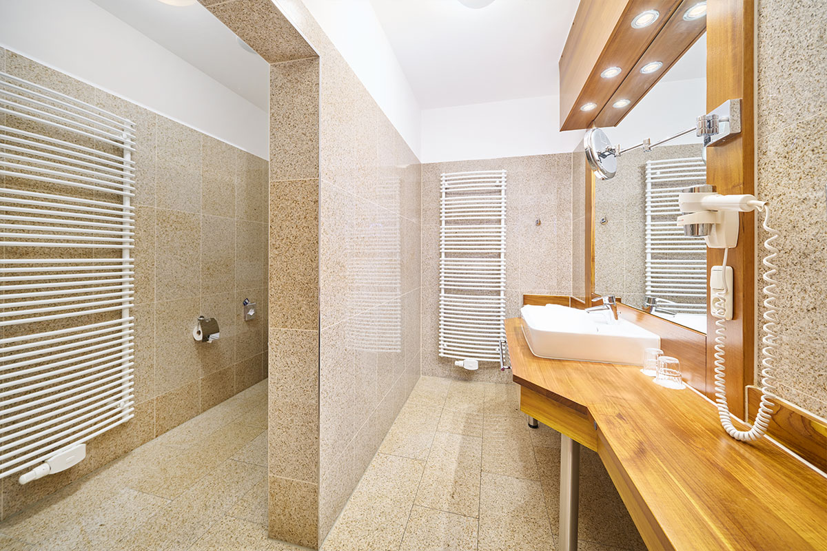 Badezimmer im Doppelzimmer Promenade der Strandvilla Viktoria mit Waschtisch, Spiegel, Handtuchwärmer und Natursteinfliesen.