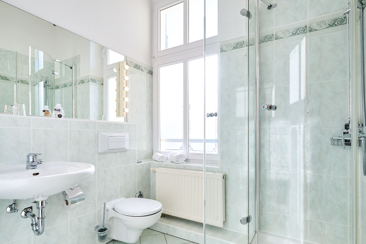 Helles Badezimmer im Einzelzimmer in der Strandvilla Viktoria mit Glasdusche, WC, Waschbecken, Spiegel und Tageslichtfenster.