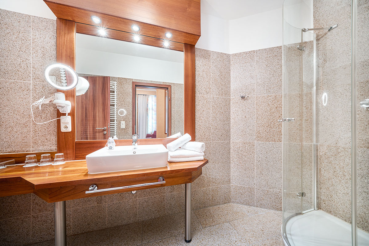 Modernes Bad im Familienzimmer in der Strandvilla Viktoria mit Holzwaschtisch, großem Spiegel, Handtüchern und Dusche.