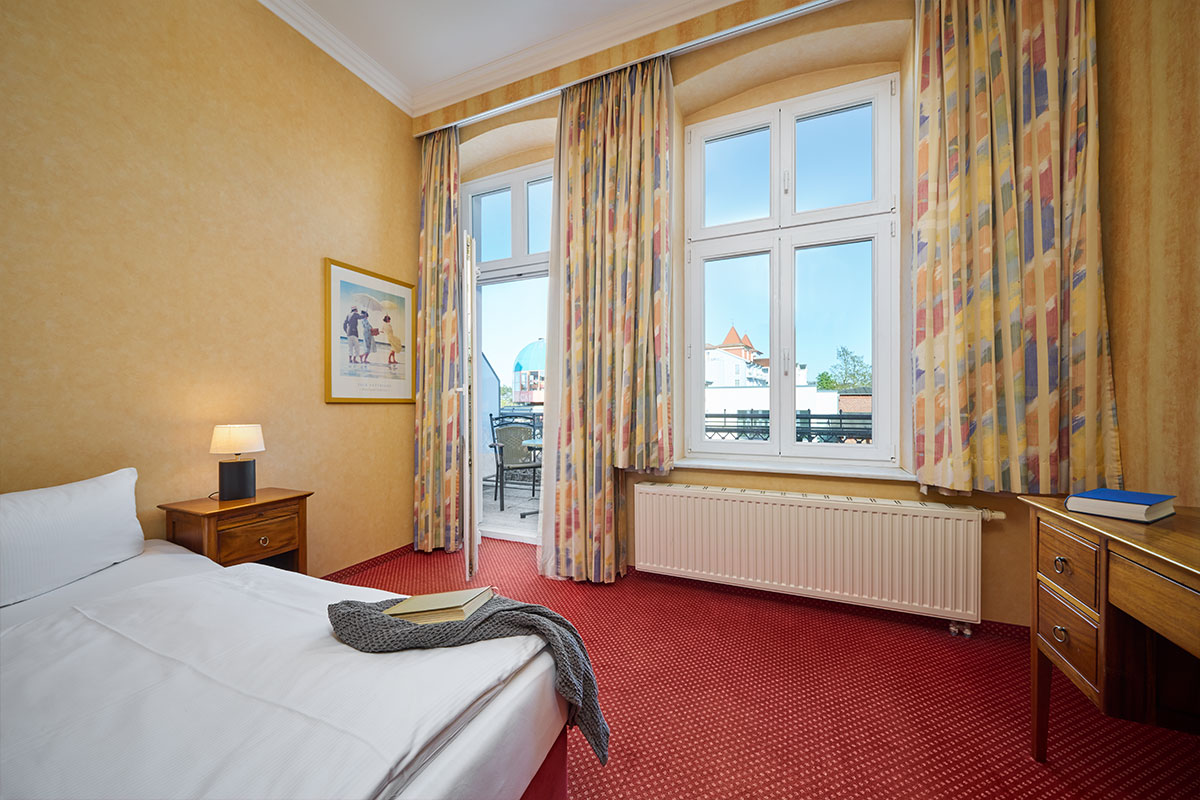 Familienzimmer in der Strandvilla Viktoria mit Doppelbett, geöffneter Balkontür und Ausblick auf die Promenade auf Usedom.