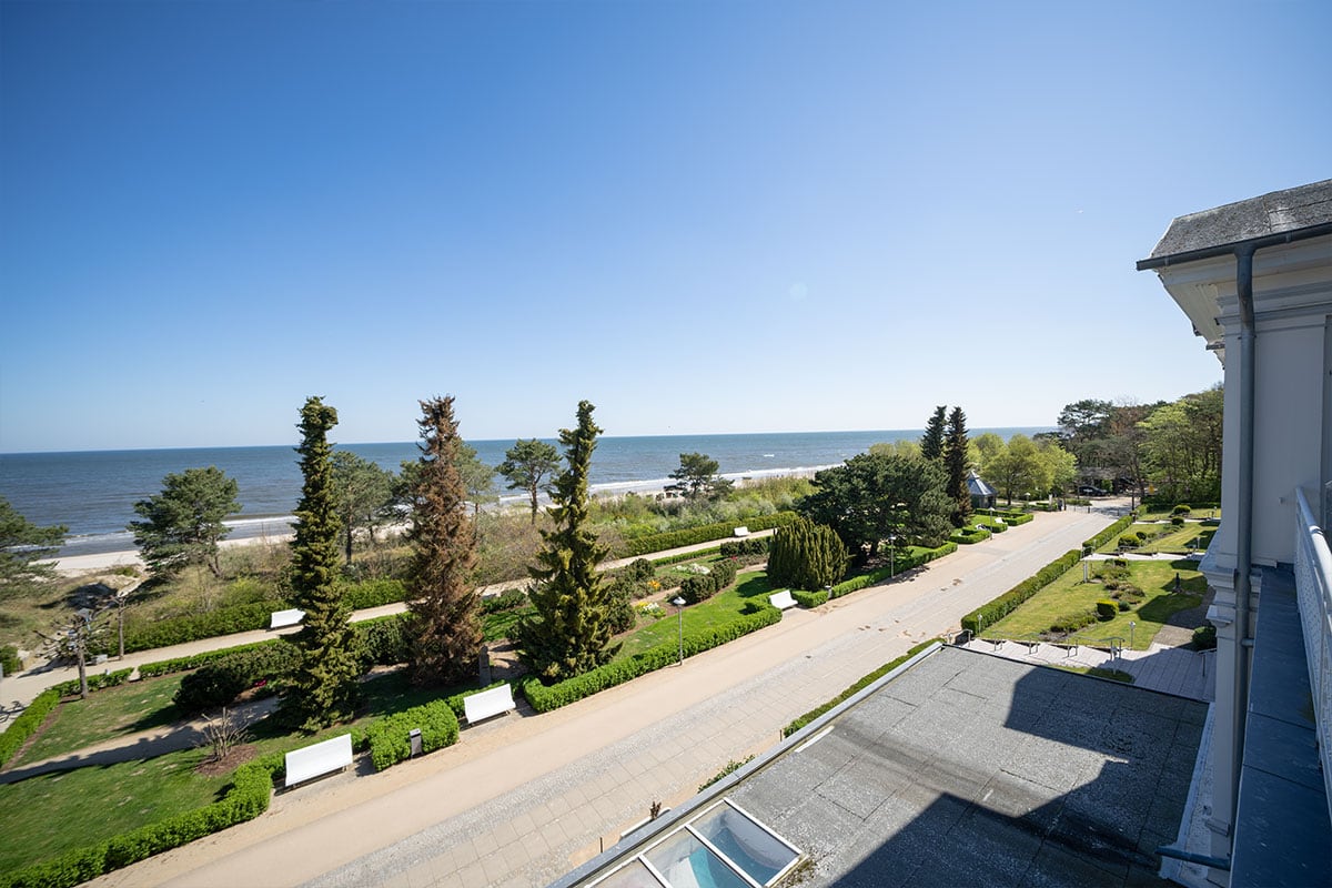 Ausblick auf die Ostsee mit Promenade, Bäumen und Strand vom Balkon der Strandvillen Wald&See in Zinnowirtz auf Usedom.