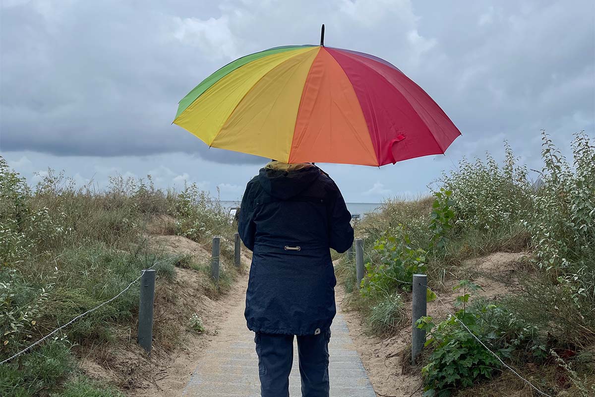 Person mit buntem Regenschirm am Strandaufgang bei Zinnowitz auf Usedom, unterwegs bei Regenwetter im Herbsturlaub