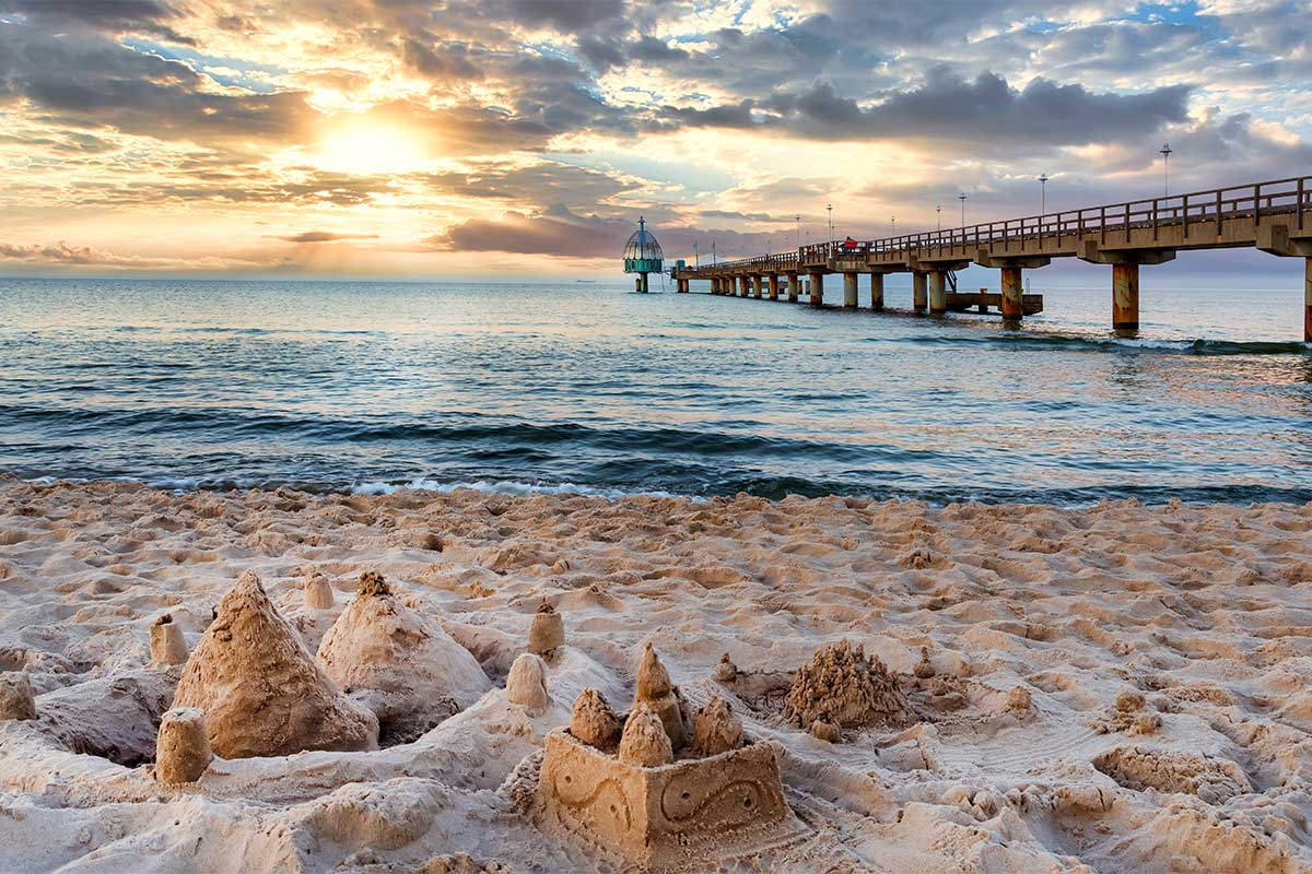 Sandburg am Strand vorm Strandkorb mit Blick auf die Seebrücke bei Sonnenuntergang auf Usedom.