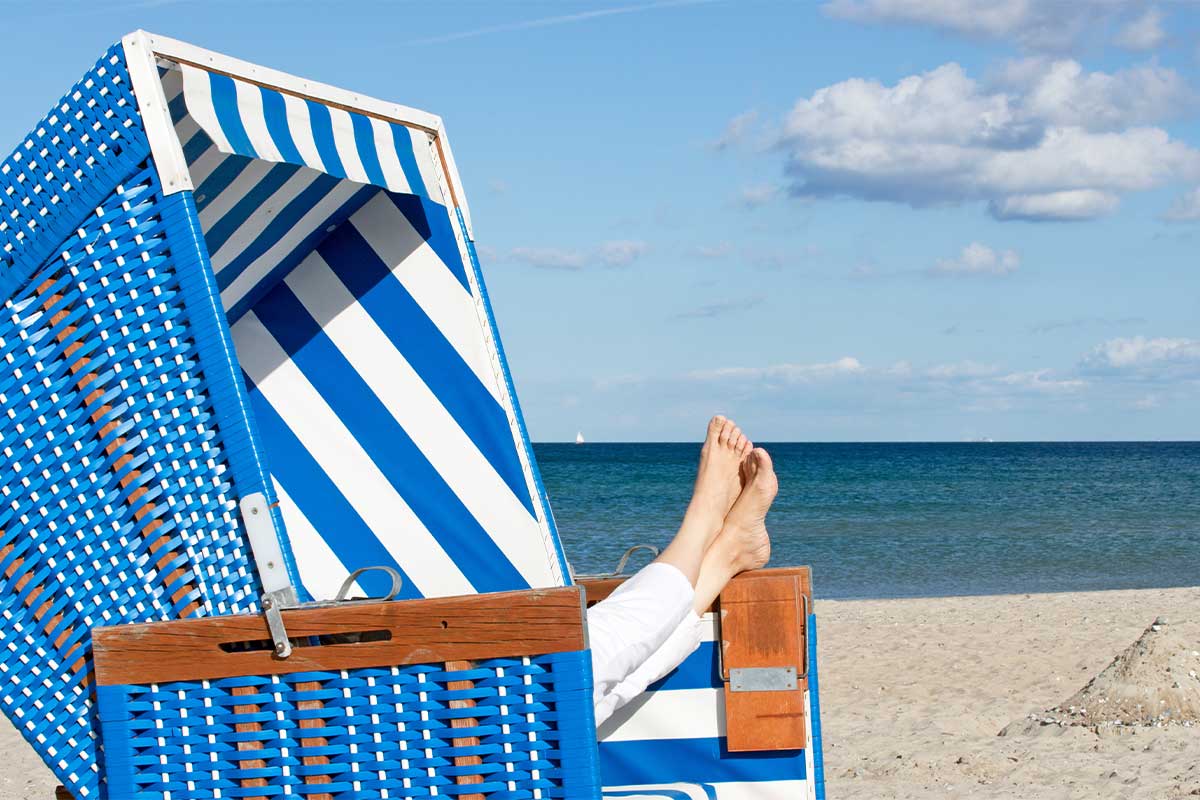 Person im Sommerurlaub auf Usedom streckt die Füße aus einem blauen Strandkorb direkt am Sandstrand von Zinnowitz