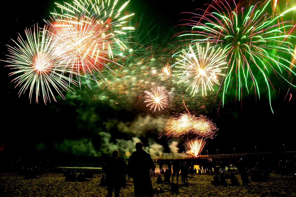 Farbenfrohes Silvesterfeuerwerk über dem nächtlichen Strand von Zinnowitz mit feiernden Urlaubsgästen.
